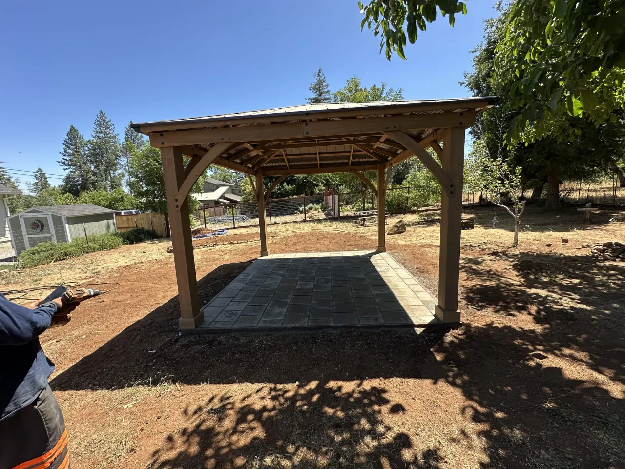 Wood pergola over a finished paver patio in a large backyard