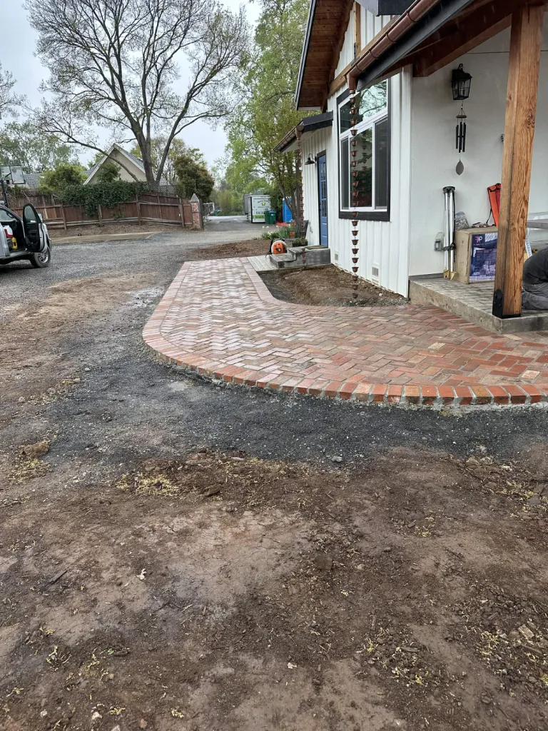 Curved brick paver walkway and entry landing in front of a white farmhouse
