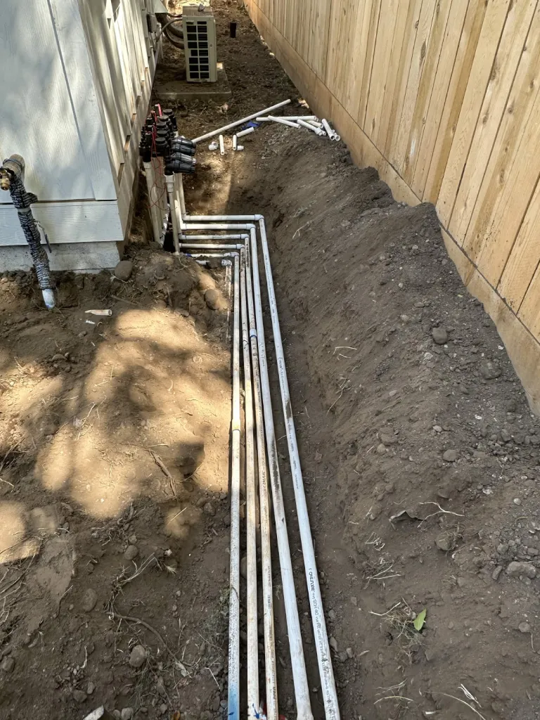 PVC irrigation lines manifolded along a house foundation in an open trench