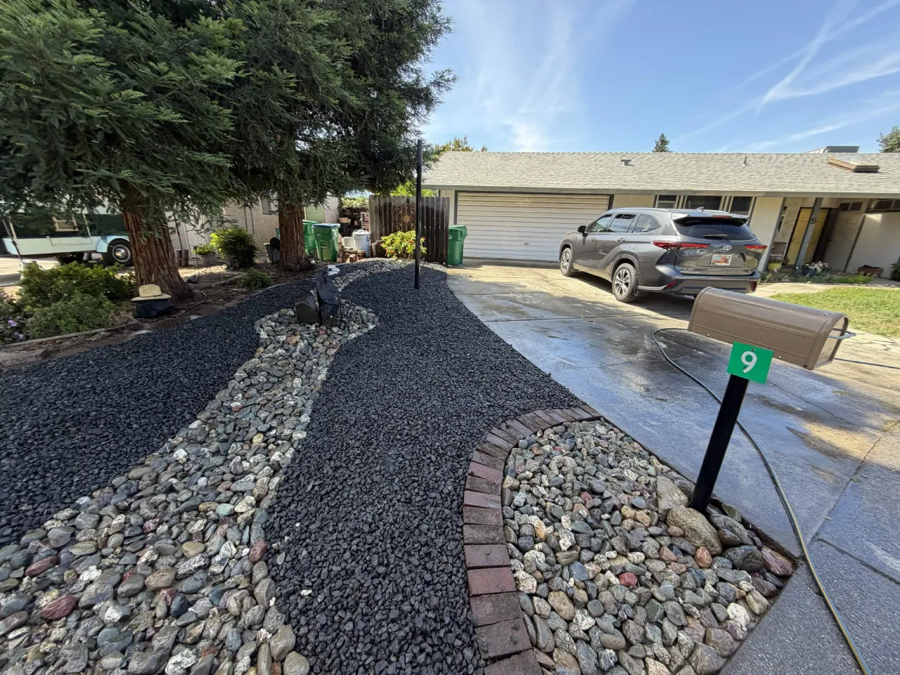 Completed front yard with black gravel beds, river rock channel and brick edging