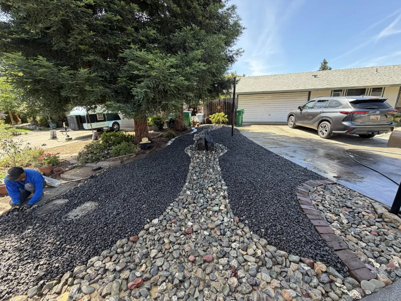 Front yard drought-tolerant install with black gravel and a river rock drainage channel