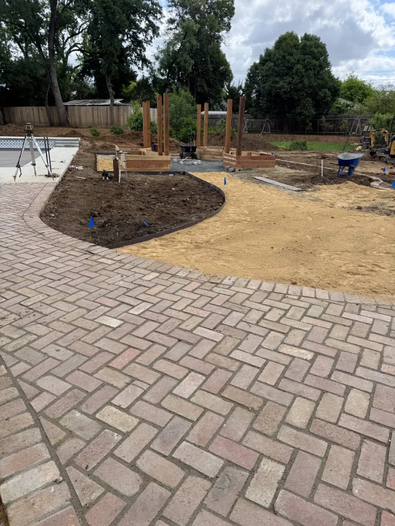 Paver patio beside a pool with timber framing and retaining walls under construction